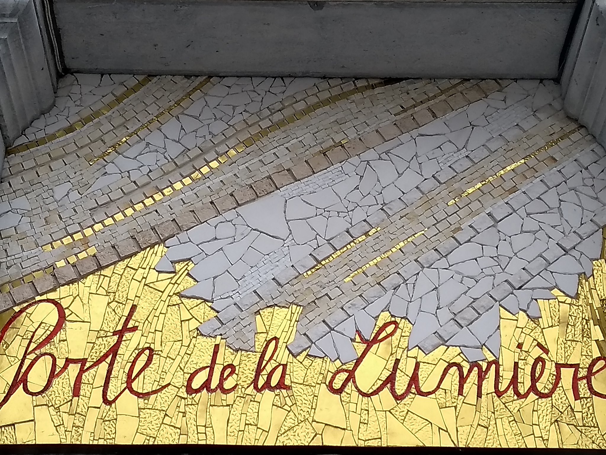 Mosaïque au sol représentant des feuilles dorées traversées de lignes de lumière, avec l’inscription « Porte de la Lumière », évoquant un passage symbolique et spirituel.