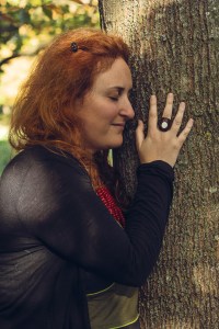 Praticienne holistique à Lille en connexion avec la nature, femme aux cheveux roux posant les mains sur un arbre lors d’un accompagnement bien-être et énergétique en plein air.