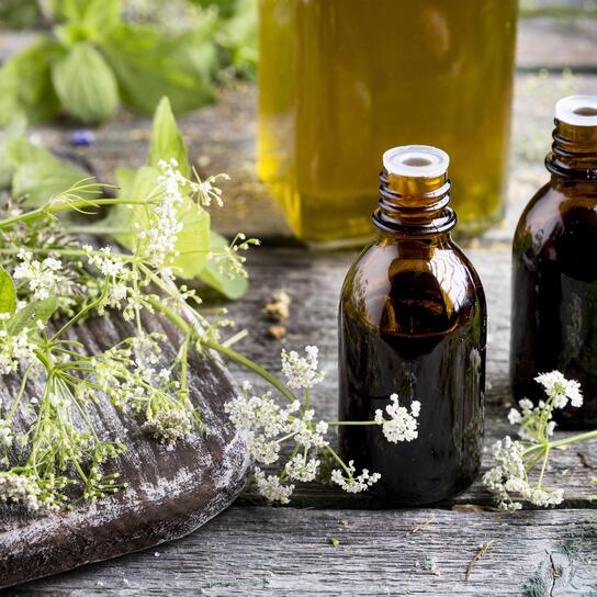 Flacons d’huiles essentielles naturels avec plantes médicinales et huile végétale, utilisés en aromathérapie, sur une table rustique – image liée à une formation sur les huiles essentielles dans le Nord.