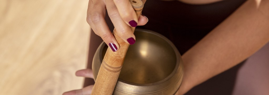 Gros plan sur une personne faisant chanter un bol tibétain avec un maillet en bois, illustrant une pratique de sonothérapie dans un cadre de formation pour praticiens bien-être